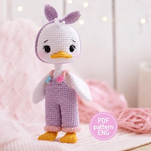 Puede incluir: Una muñeca de pato tejida a ganchillo con hilo blanco, que lleva un peto lavanda con botones de flores rosas y azules, una diadema lavanda con orejas de conejo y pies amarillos. La muñeca tiene ojos bordados negros y un pico amarillo. Texto PDF pattern ENG.