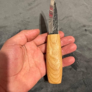 Puede incluir: Un peque&ntilde;o cuchillo artesanal con un mango de madera clara y una hoja plateada. La hoja tiene una superficie texturizada. El cuchillo est&aacute; dise&ntilde;ado para tareas de corte de precisi&oacute;n.