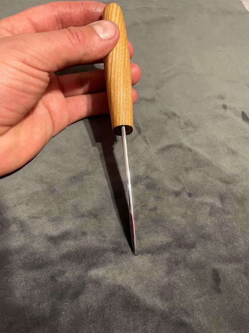 Puede incluir: Un picahielos con mango de madera clara y hoja de acero pulido. El mango es cil&iacute;ndrico, con una virola de metal oscuro. La hoja es fina y termina en punta. Longitud total aproximada de 15 cm.
