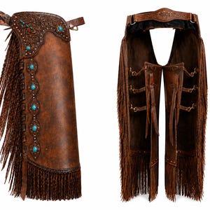 May include: Brown leather chaps featuring intricate floral tooling on the yoke, turquoise stone accents, and long fringe along the sides. The design includes adjustable buckle straps on the back and a belt-style waist closure with metal hardware.