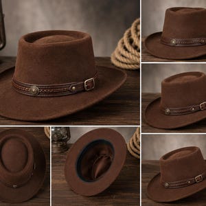 May include: A brown felt hat featuring a flat crown and a wide brim. The hat is accented with a dark brown leather band that includes a braided detail, a metallic circular stud, and a small adjustable metal buckle on the side of the crown.