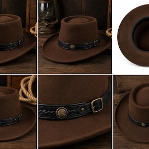 May include: A brown felt hat with a flat crown and a wide brim. The hat features a black leather band decorated with a braided texture, a central circular antique brass-toned metal stud, and a matching brass-toned metal buckle adjustment.