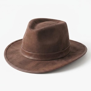 May include: A dark brown fedora hat with a matte, suede-like texture. The hat features a pinched crown and a wide, structured brim. A matching dark brown leather band encircles the base of the crown, providing a clean, uniform appearance.
