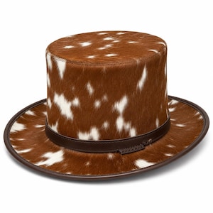 May include: A top hat featuring a brown and white cowhide pattern with a short, flat crown and a wide brim. The base of the crown is encircled by a dark brown leather band, and the edge of the brim is finished with a matching dark brown leather trim.
