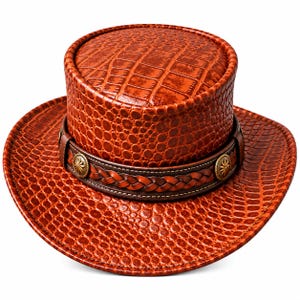Peut inclure: Un chapeau marron avec un motif texturé en peau de crocodile. Le chapeau présente une bande en cuir marron foncé ornée d'une lanière en cuir tressé et de deux ornements métalliques circulaires avec un motif en étoile au centre.