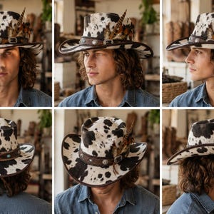 May include: A cowhide print cowboy hat featuring a dark brown leather band with silver-toned metal studs and a buckle. The hat is adorned with a cluster of brown and black feathers tucked into the side of the band, showcasing a patterned texture.