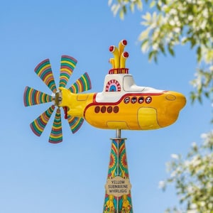 Peut inclure: Un moulin à vent en forme de sous-marin jaune avec une hélice multicolore et une base décorative. Le sous-marin a un dessus blanc et des accents rouges. La base porte l'inscription "YELLOW SUBMARINE WHIRLIGIG".