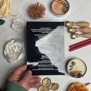Puede incluir: Una tarjeta de invitación de boda rectangular en blanco y negro con texto blanco que presenta los nombres Mario y Jessica, la fecha 26 de julio de 2025 y detalles de la ceremonia, rodeada de tres sellos de madera, dos barras de cera roja y dos velas.
