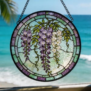 May include: Round stained glass window with a black metal frame and chain. The window features a design of purple and white wisteria flowers with green leaves. The background is a light blue and green color.