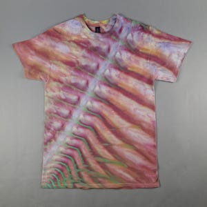May include: A short-sleeve crew neck t-shirt featuring a tie-dye pattern with diagonal bands of pink, orange, yellow, and light green colors. The design radiates from a central diagonal line, creating a soft, blended effect across the fabric.