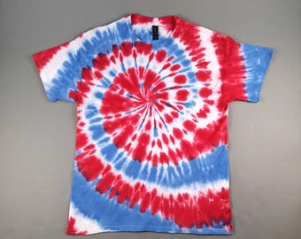 May include: A red, white, and blue tie-dye t-shirt. The spiral design features concentric circles of red, white, and blue. The shirt has short sleeves and a crew neck. The shirt is made of a soft material.