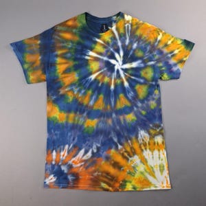 May include: A short-sleeve crew neck t-shirt featuring a spiral tie-dye pattern in shades of deep blue, bright orange, yellow, and white. The design radiates from an off-center point, creating a swirling effect across the fabric surface.
