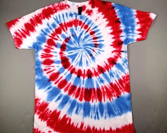 May include: A short-sleeved t-shirt with a spiral tie-dye pattern in red, white, and blue. The design radiates from the center, creating a bold and colorful effect. The shirt is made of a soft material and is suitable for casual wear.