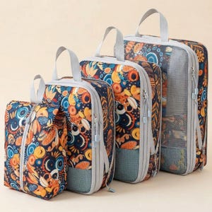 May include: A set of four travel packing cubes in varying sizes. The cubes feature a navy blue background with a colorful floral pattern in orange, yellow, and blue. Each cube has a gray handle and zipper.