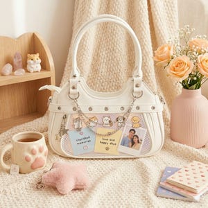 May include: White handbag with a rounded shape, featuring a mesh panel with dog illustrations and a photo. The bag has silver chain accents and a star charm. A mug with paw prints, a pink star-shaped item, and a vase of flowers are also present.