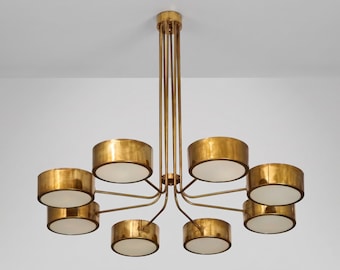 May include: A brass chandelier with eight cylindrical shades. The shades are arranged in a circular pattern, each with a white interior. The fixture is suspended from the ceiling by multiple brass rods.