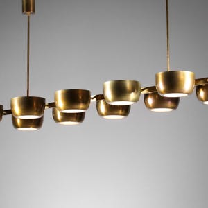 Könnte beinhalten: Eine moderne, messingfarbene Hängeleuchte mit acht schalenförmigen Leuchten. Die Leuchten sind an einer zentralen Stange aufgehängt und horizontal angeordnet. Das Design ist schlicht und minimalistisch, passend für verschiedene Einrichtungsstile.