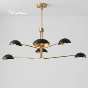 Könnte beinhalten: Eine moderne Deckenleuchte mit goldener Oberfläche und schwarzen Schirmen. Die Leuchte hat eine zentrale Nabe mit mehreren Armen, die sich nach außen erstrecken und jeweils einen schwarzen, halbkreisförmigen Schirm mit goldener Innenseite halten. Sie hängt von der Decke.