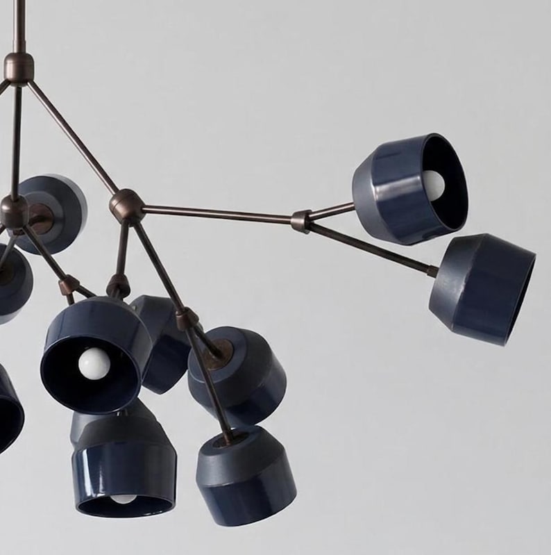 May include: A modern chandelier with a bronze-colored frame and multiple navy blue cone-shaped shades. Each shade houses a white light bulb. The fixture has a unique, artistic design, suitable for interior lighting.