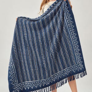 May include: A rectangular throw blanket in deep navy blue featuring a repeating white geometric pattern of vertical stripes and triangles. The blanket is framed by a wide decorative border and finished with long navy blue fringe on the edges.