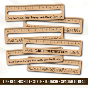 May include: A collection of light-colored wooden line reader rulers, each featuring a horizontal cutout slot and a 15 cm measurement scale. The rulers display various engraved designs, including space motifs, birds, and text like Keep Learning, Keep Trying, and Never Give Up.