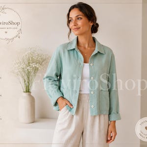 Puede incluir: Chaqueta de lino verde claro con cuello y cierre de botones, combinada con pantalones beige. La chaqueta tiene dos bolsillos delanteros. La imagen también presenta un jarrón con flores blancas y el texto "FloviroShop".