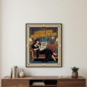 Puede incluir: Una impresión artística enmarcada que presenta a una mujer con un vestido negro leyendo un periódico con el titular "Gossip Scandal!". La impresión tiene un estilo de cómic vintage con el texto "I Heard That About Myself Too". La obra de arte está ambientada en una habitación con un sofá rojo.