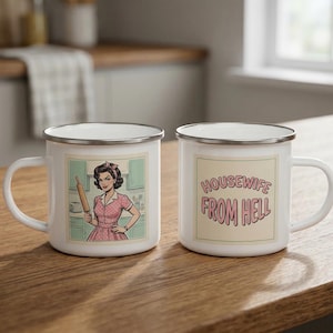 May include: Two white enamel mugs with silver rims. One mug features a retro illustration of a woman holding a rolling pin. The other mug has the text "Housewife From Hell" in pink and purple.