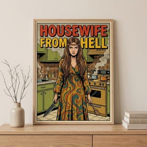 May include: Framed art print featuring a retro illustration of a woman in a kitchen, holding a knife and a wooden spoon. The print has the text "HOUSEWIFE FROM HELL" in bold letters. The woman is wearing a long, patterned dress.