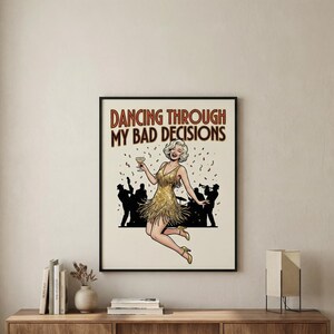 May include: A framed poster with the text "Dancing Through My Bad Decisions." The artwork features a cartoon woman in a gold dress holding a cocktail, with a crowd of silhouettes in the background. The poster is in a black frame.