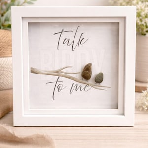 Puede incluir: Obra de arte enmarcada en blanco con el texto "Talk to me" y dos pájaros de piedra posados en una rama. La obra de arte está sobre un fondo blanco, creando una estética minimalista y natural.