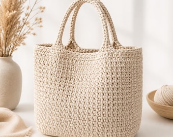 Op de afbeelding: Een beige gehaakte tote bag met twee geïntegreerde handvatten, voorzien van een dicht, gestructureerd steekpatroon. De tas heeft een rechthoekige bodem en een open ontwerp, vervaardigd van lichtgekleurd garen in een neutrale, effen tint.