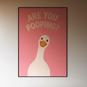 Puede incluir: Interior de dormitorio con un p&oacute;ster enmarcado con un ganso blanco y el texto "ARE YOU POOPING?" sobre un fondo rosa. Una cama con una colcha gris oscuro est&aacute; en primer plano. La luz natural entra por grandes ventanas.