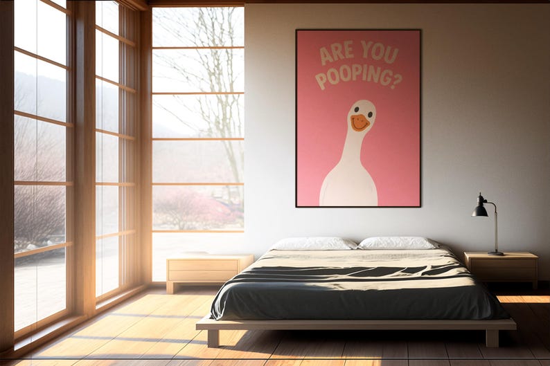 Puede incluir: Interior de dormitorio con un p&oacute;ster enmarcado con un ganso blanco y el texto "ARE YOU POOPING?" sobre un fondo rosa. Una cama con una colcha gris oscuro est&aacute; en primer plano. La luz natural entra por grandes ventanas.