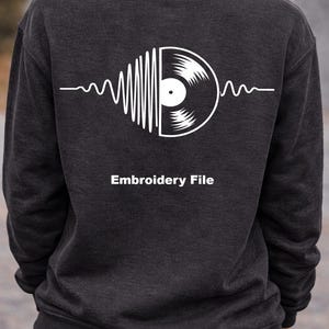 Op de afbeelding: Donkergrijze sweatshirt met een witte afbeelding van een vinylplaat en geluidsgolven. De tekst "Embroidery File" staat onder de afbeelding. De sweatshirt wordt door een persoon gedragen.