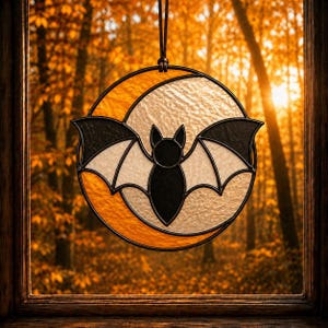 May include: A circular stained glass suncatcher featuring a black bat silhouette centered against a textured white moon and a vibrant orange crescent moon background, all held together by dark metal lead lines and suspended by a leather cord.