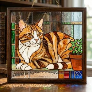 Pode incluir: Painel de vitral com um gato malhado em tons de laranja, castanho e branco, com uma pequena planta em vaso. A obra de arte é emoldurada em uma moldura de madeira escura e pendurada por uma corrente dourada.
