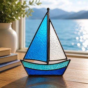 Peut inclure: Un voilier en vitrail composé d'une voile bleue texturée, d'une voile blanche et d'une coque formée d'une bande bleu clair sur une base bleu foncé. L'objet est assemblé avec une armature en métal sombre et un mât central surmonté d'une bille.