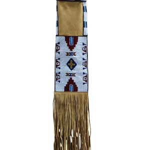 May include: A long, rectangular beaded bag with a tan leather pouch and fringe. The bag has a white background with geometric patterns in red, blue, and black beads. The fringe is a light brown colour.