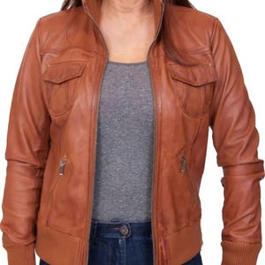May include: A brown leather jacket with a zip-up front, two chest pockets, and ribbed cuffs. The jacket has a stand-up collar and a tailored fit. The model is wearing a gray shirt and blue jeans.