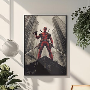 May include: Framed art print depicting Deadpool in a red suit, holding two swords, in a comic book style. The artwork is set against a backdrop of tall buildings, with a black frame.