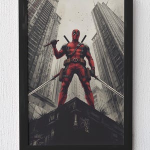 May include: Framed artwork depicting Deadpool in a comic book style. The character, in a red and black suit, holds two katanas, standing on a rooftop with a cityscape backdrop. The artwork is presented in a black frame.