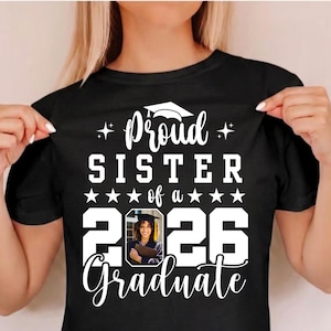 Puede incluir: Camiseta negra con texto blanco: "Orgullosa hermana de un graduado de 2026". El dise&ntilde;o incluye un gorro de graduaci&oacute;n y una foto de un graduado. La camiseta es de cuello redondo.