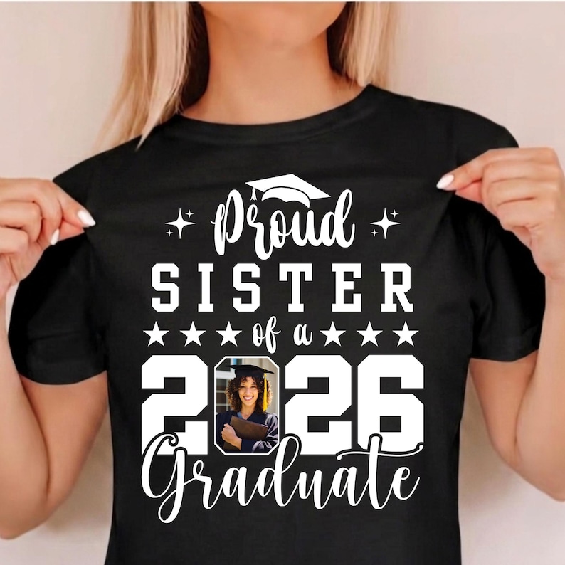 Puede incluir: Camiseta negra con texto blanco: "Orgullosa hermana de un graduado de 2026". El dise&ntilde;o incluye un gorro de graduaci&oacute;n y una foto de un graduado. La camiseta es de cuello redondo.
