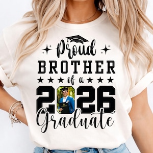 Puede incluir: Camiseta color crema con el texto "Proud Brother of a 2026 Graduate". El dise&ntilde;o incluye un gorro de graduaci&oacute;n, estrellas y una foto de un graduado con una blazer azul sosteniendo un diploma. Un regalo para un hermano orgulloso.