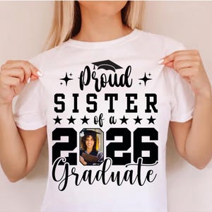 Puede incluir: Camiseta blanca con el texto negro "Proud Sister of a 2026 Graduate". El dise&ntilde;o incluye un gorro de graduaci&oacute;n, estrellas y una foto de una graduada. Un regalo para una hermana orgullosa.