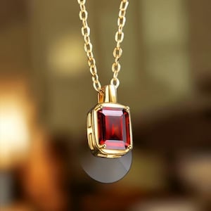 Peut inclure: Un collier en or avec un pendentif en grenat rouge profond de forme rectangulaire et taille émeraude, serti dans une monture en or poli. Le pendentif est suspendu à une fine chaîne en or à maillons ovales, mettant en valeur la pierre facettée.