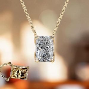 Peut inclure: Un collier à chaîne dorée avec un pendentif en pierre transparente de taille radiant rectangulaire maintenu par quatre griffes. Une vue secondaire montre le dessous du sertissage, révélant un motif ajouré géométrique.