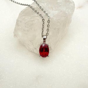 May include: A silver necklace featuring a vivid red, oval pendant. The pendant, a deep red hue, is set in a silver bezel. The delicate chain suspends the pendant, creating a classic jewellery piece.
