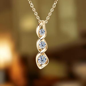 May include: A gold-toned pendant necklace featuring a vertical, twisted metal design that holds three round, clear, faceted stones arranged in a column. The pendant is suspended from a delicate, matching gold-toned chain with small, oval links.